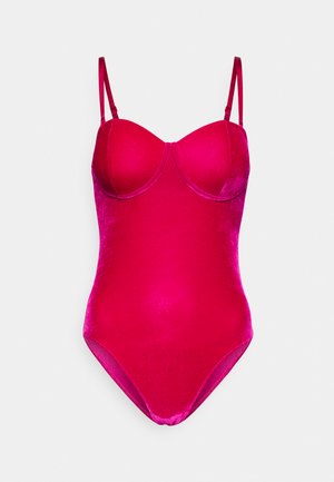Bodysuit en velours rose avec un buste structuré, des bretelles réglables et une coupe jambe haute. Texture lisse et silhouette ajustée.