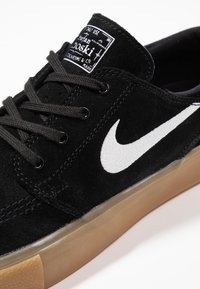 Sneaker in suede nera con swoosh bianco di Nike, lacci neri e suola in gomma. Presenta il marchio sulla linguetta e un colletto imbottito.