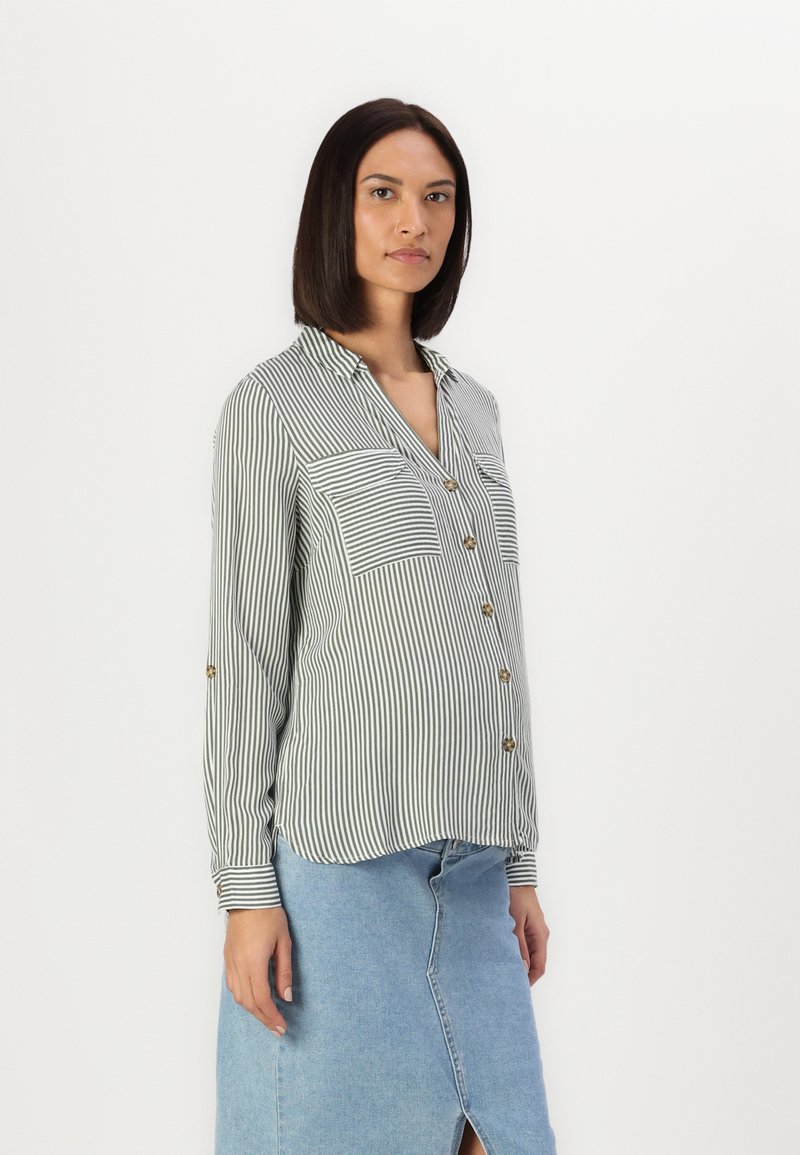 Camicia a righe verde e bianca con due tasche sul petto e bottoni dorati, abbinata a una gonna in denim azzurro chiaro.