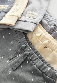 Drei Paar Kinderhosen in Grau und Creme, mit einem Punkte-Muster, Zugbändern und Etiketten mit "happy little one"-Branding.