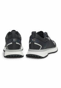 Para czarnych i szarych butów sportowych widziana z tyłu, charakteryzująca się siatkową tkaniną, paskami do zakupu i białymi, amortyzowanymi podeszwami.