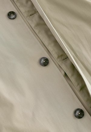 Khaki trenchcoat met een gladde textuur, voorzien van donkere knopen en subtiele stikdetails langs de sluiting en de halslijn.