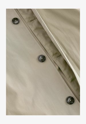 Kaki színű trench coat sima textúrával, sötét gombokkal és finom varrási részletekkel a gombolásnál és a nyaknál.