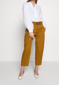 Vit långärmad blus med V-ringning och elastiska manschetter, kombinerad med högmidjade, löst sittande byxor i senapsgul färg och vita spetsiga klackar.