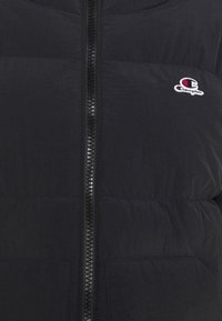 Svart puffjacka med framdragkedja och sydda paneler. Har en liten broderad logo på vänster bröstområde. Mjuk textur.