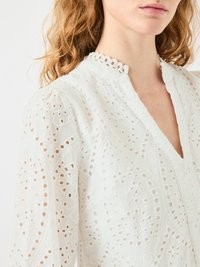 Blusa bianca ricamata con colletto alla cinese, caratterizzata da tagli dettagliati, motivi floreali e maniche leggermente voluminosi.