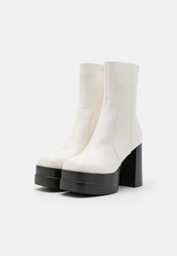 Witte leren enkelboots met een gladde afwerking, voorzien van een dikke zwarte hak en plateau, ontworpen met minimale stiksels en zonder versieringen.
