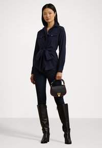 Jūras zila krekls ar pogām un sasietu priekšu, tumši zilo džinsu bikses, ceļgala augstuma melni ādas zābaki un neliela melna rokassoma ar zelta detaļām un sarkanām akcentiem.