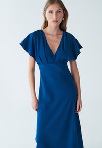 Modré šaty s krátkym rukávom, hlbokým výstrihom do V, priliehavým živôtikom a voľnou sukňou. Hladká textúra s mierne lesklým povrchom.
