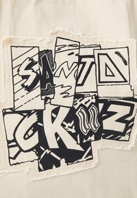 Tissu blanc présentant un design graphique noir avec différentes lettres et formes stylisées, certaines avec des bords rugueux et un placement en chevauchement.
