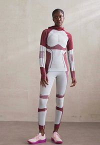 Atlétikai szett, amely egy bordó és fehér, kapucnis, testhezálló hosszú ujjú felsőből és hozzá illő leggingsből áll, rugalmas anyagból készült, geometrikus mintákkal.