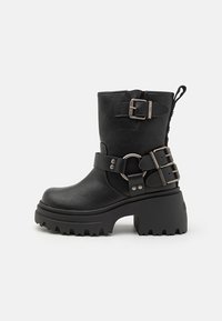 Black leather ankle boot with a chunky sole, buckle and strap accents, and a textured finish. Features a pull tab for easy wear.
