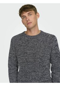 Gebreide crew neck trui in donker marineblauw met een lichtgrijs textuurpatroon. Ribbelboord bij de hals en manchetten. Zacht, mediumgewicht materiaal; casual pasvorm.
