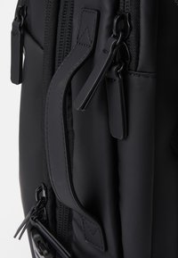 Mochila negra hecha de tejido texturizado, con cremalleras, un asa superior y un diseño estructurado con acentos cosidos.