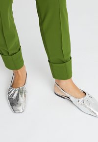 Silberne Flats mit einer strukturierten, glänzenden Oberfläche und einem gathers Design, kombiniert mit grünen, umgeschlagenen Hosen.