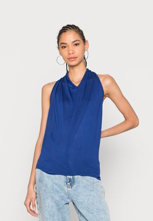 Top azul sem mangas em tecido suave com decote drapeado, combinado com jeans de denim leve de cintura alta.