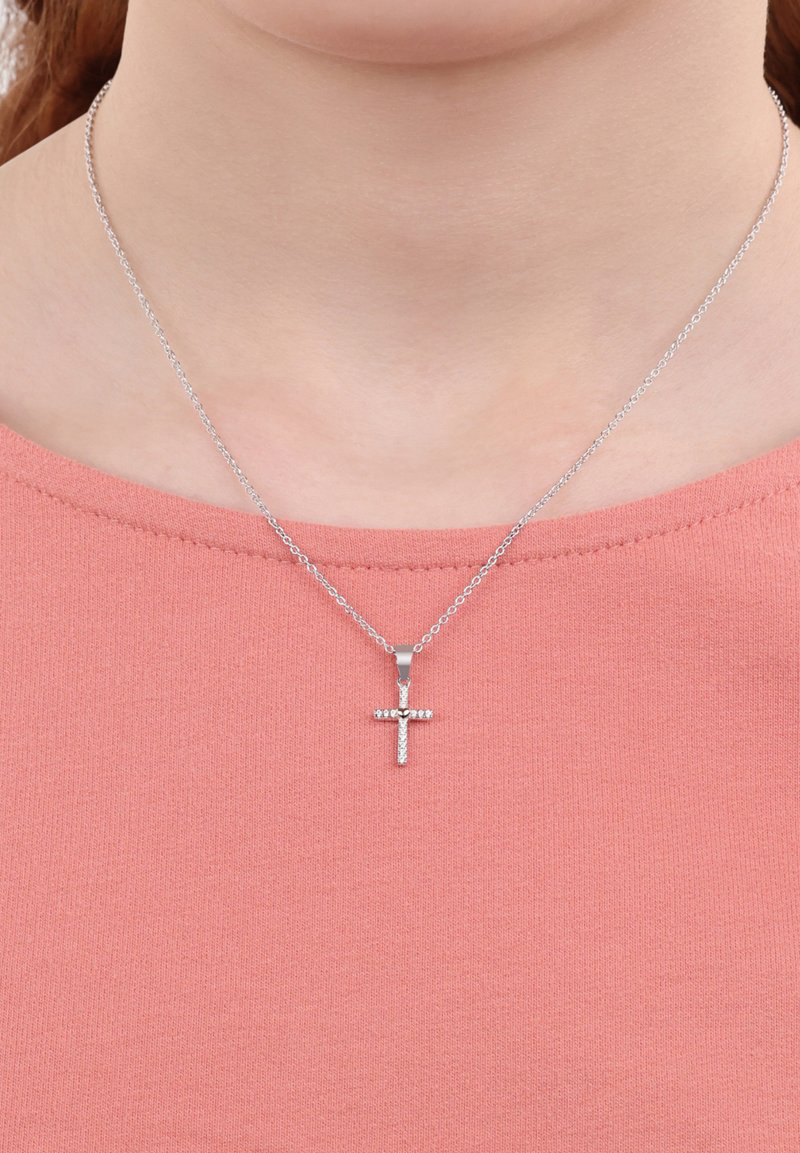 Collana a croce d'argento con piccole pietre trasparenti su una catena fine, indossata sopra una camicia rosa testurizzata.