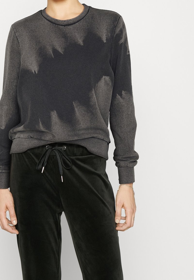 Sudadera gris oscuro con un sutil patrón de tie-dye. Tejido suave y puños acanalados. Combinada con pantalones de terciopelo verde oscuro con cintura elástica y cordón.