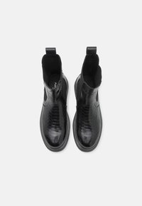 Svarta chelsea-boots i glänsande, texturerat läder med ormskinnsmönster, med elastiska sidopaneler och en dragflik.