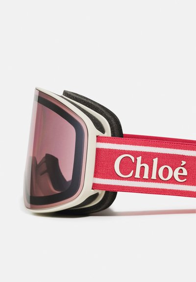 Skidglasögon med en vit ram, rosa spegelglas och ett röd band med vita ränder och "Chloé"-logotyp. Texturerad insida för komfort.
