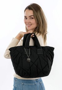 Black quilted tote bag with dual handles, featuring a metal charm and square accents. Fabric is soft with a textured pattern.