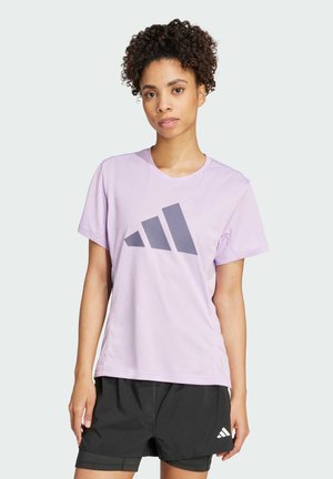 Vaalean violetti urheilupaita, jossa on suuri harmaa Adidas-logo. Paidassa on lyhyet hihat ja pyöreä kaula-aukko, ja se on valmistettu hengittävästä kankaasta.
