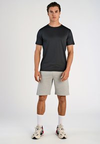 Svart t-shirt med kort ärm, gråa shorts, atletisk passform. Slät struktur, rund halsdesign, bärs med vita strumpor och mångfärgade sneakers.