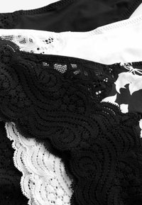 Lingerie met kantafwerking in zwart en wit, met ingewikkelde golfpatronen en contrasterende texturen. Gladde stof mengt zich met delicate kantaccenten.