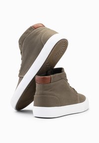 Zapatillas altas de lona verde oliva con suelas de goma blanca, que presentan detalles en cuero marrón en el talón y un patrón de textura en la suela.