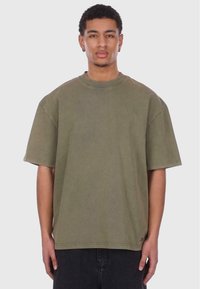 Oliven grøn oversized T-shirt med rund halsudskæring, korte ærmer og en blød tekstur, parret med sorte bukser. Simpelt design uden udsmykninger.