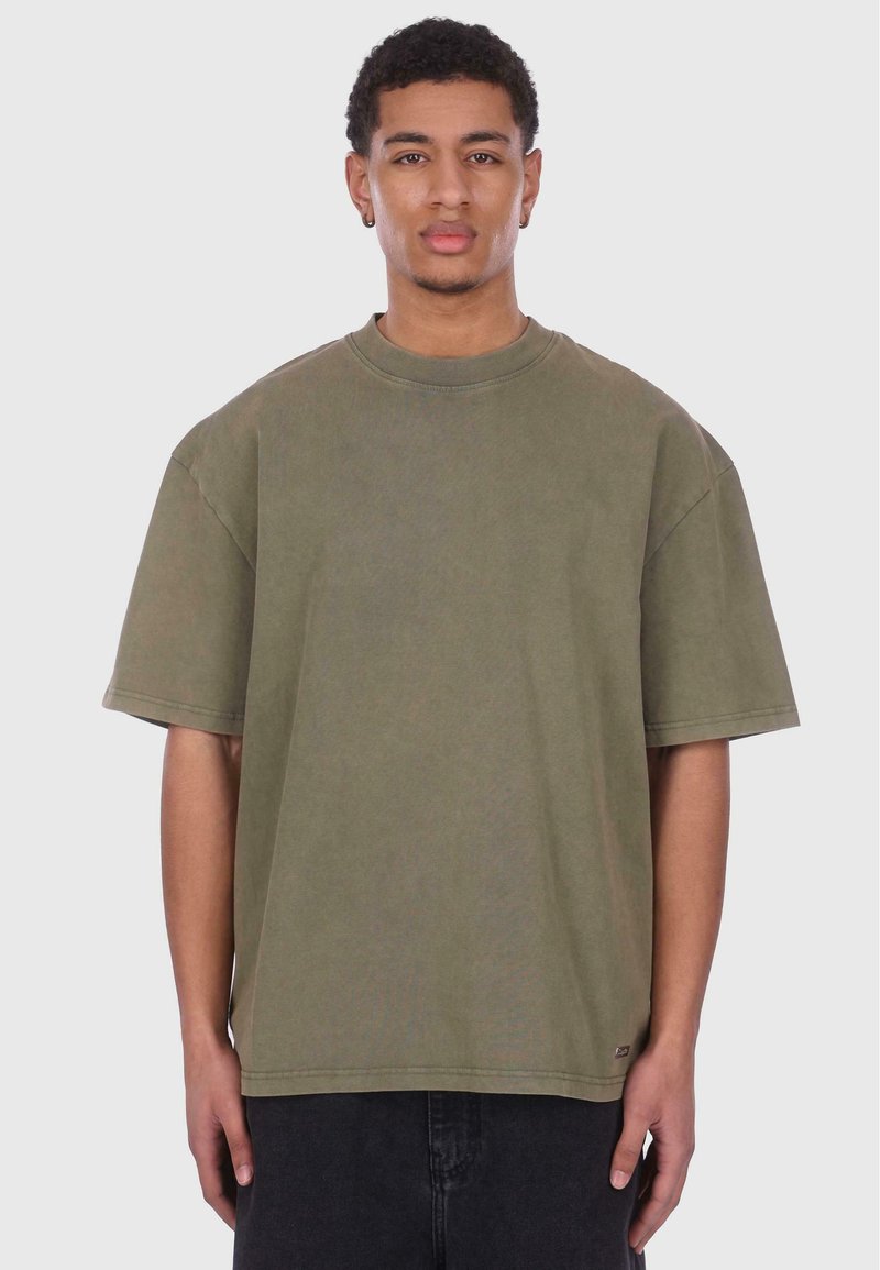 Oliven grøn oversized T-shirt med rund halsudskæring, korte ærmer og en blød tekstur, parret med sorte bukser. Simpelt design uden udsmykninger.