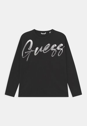 Sort langærmet skjorte med stort sølvmetallic "Guess" logotekst over brystet, vist på en ensartet lys baggrund.