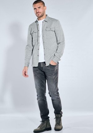 Gray button-up shirt with two chest pockets, paired with a white T-shirt, dark gray jeans, and olive green lace-up boots.