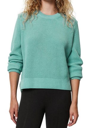 Kvinde iført en ribstrikket mintgrøn sweater med op-rullede ærmer og sorte bukser, vist fra nakke til hofter.