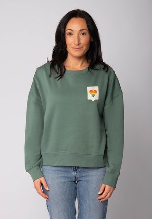 Grüner Sweatshirt mit lockerer Passform, gerippten Bündchen und Saum. Mit einem strukturierten Herz-Patch in Regenbogenfarben auf der Brust. Aus weichem Baumwollgemisch.