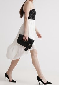 Strapless jurk met een zwarte pailletten top en een witte vloeiende rok. Zwarte clutch tas met franjeretail. Zwarte puntige hakken.