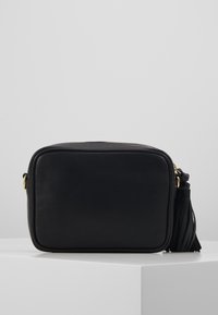 Czarna prostokątna skórzana torba na ramię z złotymi detalami i dużym skórzanym chwostem przy suwaku, umieszczona na białej powierzchni.