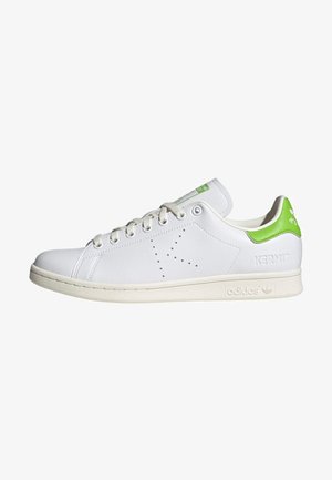 Witte lage Adidas sneaker met een groene hieltab, geperforeerde "K" aan de zijkant, en "Kermit" gegraveerd nabij de hiel.