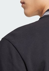 Black cotton jacket featuring a textured surface and a striped ribbed collar. Close-up view of the shoulder and neck area.