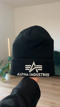 Gorro de malha preto com punho dobrado. Apresenta um logótipo prateado bordado da "Alpha Industries" e detalhes gráficos na frente.