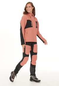 Waterdichte roze en zwarte outdoorjas met capuchon, ritszakken en bijpassende broek met meerdere zakken en verstevigingspanelen.