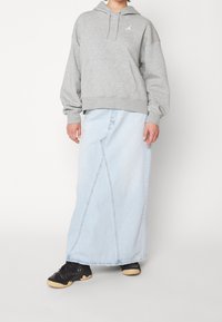 Sudadera gris con capucha y un logo, combinada con una falda vaquera larga azul claro con un detalle de costura. Se lleva con zapatillas deportivas negras.