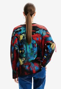Pull multicolore présentant un motif rouge, bleu, jaune et noir. Coupe ample avec des manches longues et un tissu texturé.