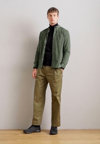 Camisa verde de botones, cuello de tortuga negro, pantalones caqui y zapatos negros. Corte ajustado; textura suave. Presenta un look casual y en capas.