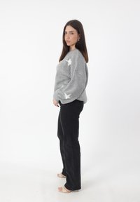 Maglione grigio a maglia grossa con motivi a stelle bianche, abbinato a jeans neri a campana e sandali con tacco color nudo. Texture liscia e vestibilità rilassata.