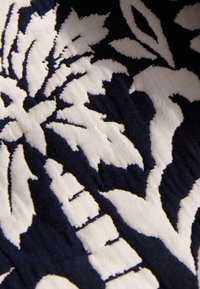 Baumwollstoff mit einem großen, auffälligen Blumenmuster in Marineblau und Weiß, mit detaillierten Verzierungen und einer strukturierten Oberfläche.