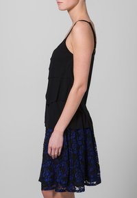 Top de tirantes delgados en negro con capas, encima de una falda hasta la rodilla con patrones de encaje floral azul. Tejido suave, diseño casual.