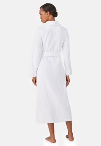 Biały szlafrok wykonany z teksturowanej tkaniny, z kołnierzem szalowym, długimi rękawami i paskiem w talii, zaprojektowany z myślą o komforcie.