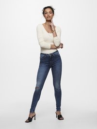 Kremfarget ribbestrikket langermet topp kombinert med slitte mørkeblå skinny jeans og svarte åpen-tå hæler. Enkle smykker som aksenter.