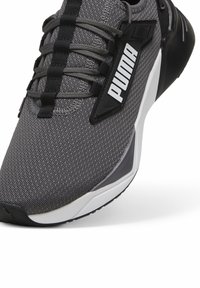 Zapatilla deportiva gris con upper de malla, que presenta cordones negros, un logo blanco prominente y una suela texturizada para agarre y soporte.